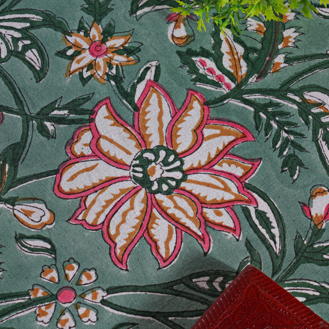 Close-up of a floral patterned fabric with pink and orange flowers on a green background.