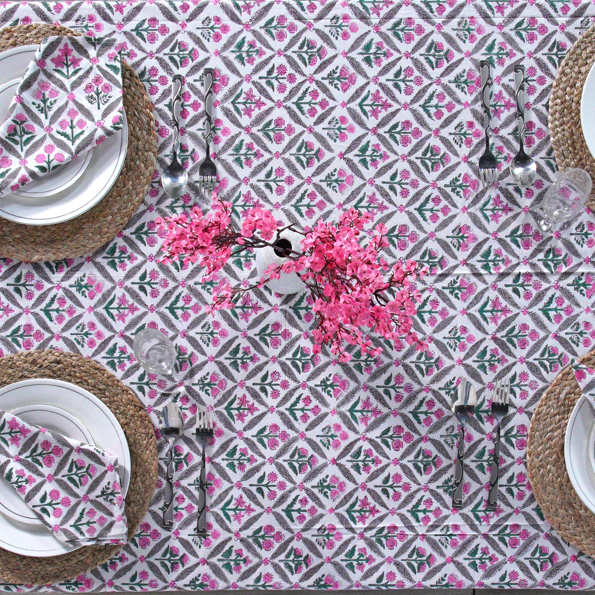Table setting with a pink and gray patterned tablecloth, plates, napkins, and cutlery.
