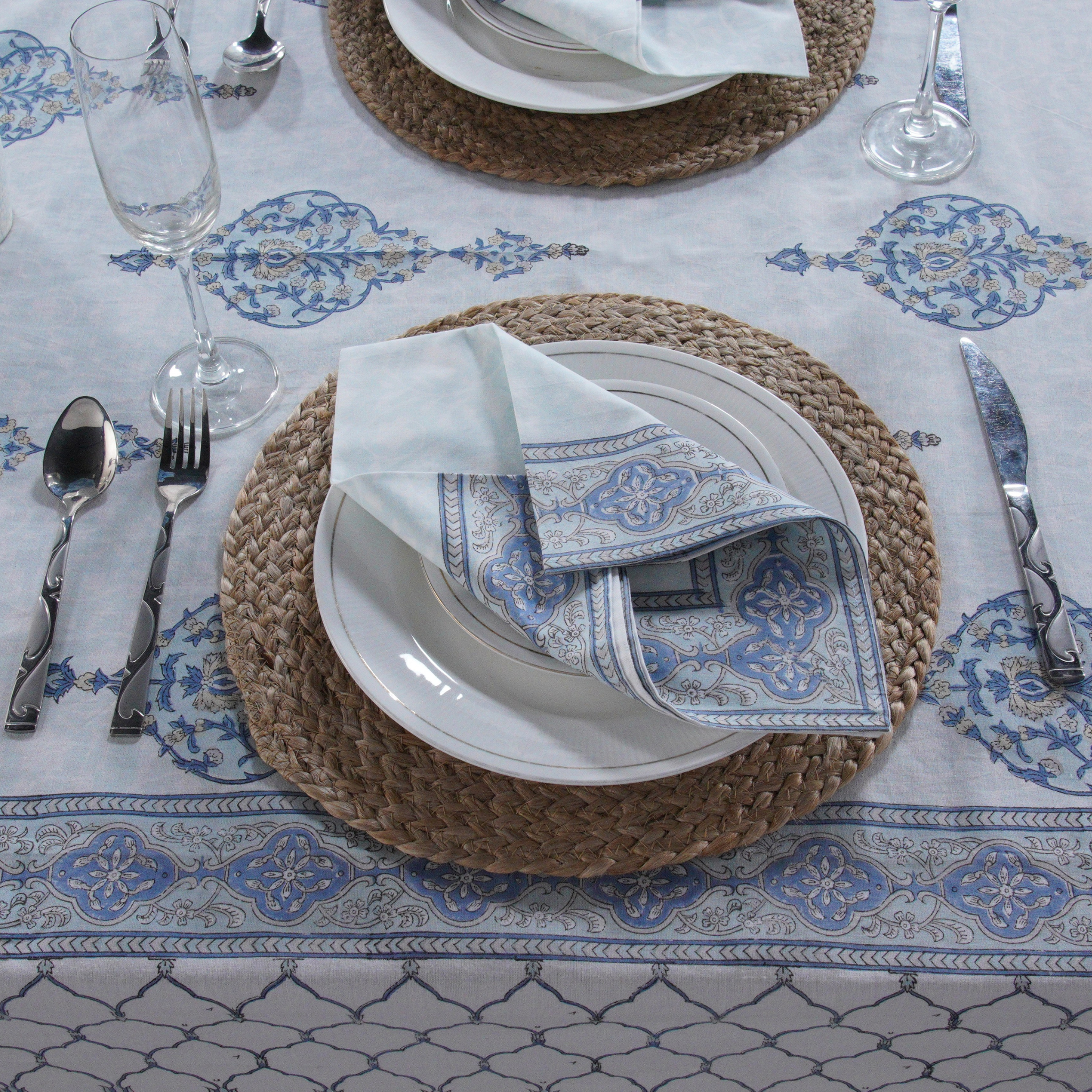 Table setting with white plates, blue patterned napkins, and silverware on a decorative tablecloth.