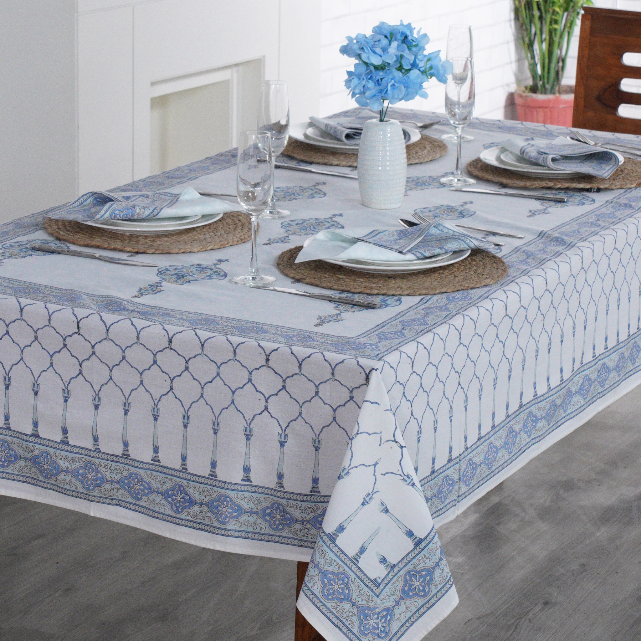 Dining table set with a blue and white patterned tablecloth, glasses, and plates.