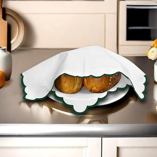 Two baked goods on a decorative plate with a white cloth draped over it, set against a kitchen counter.