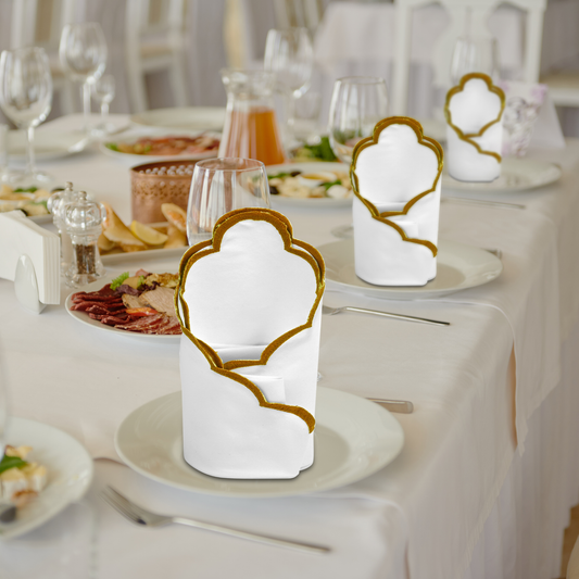 Decorative white napkins with gold borders on a set dining table.