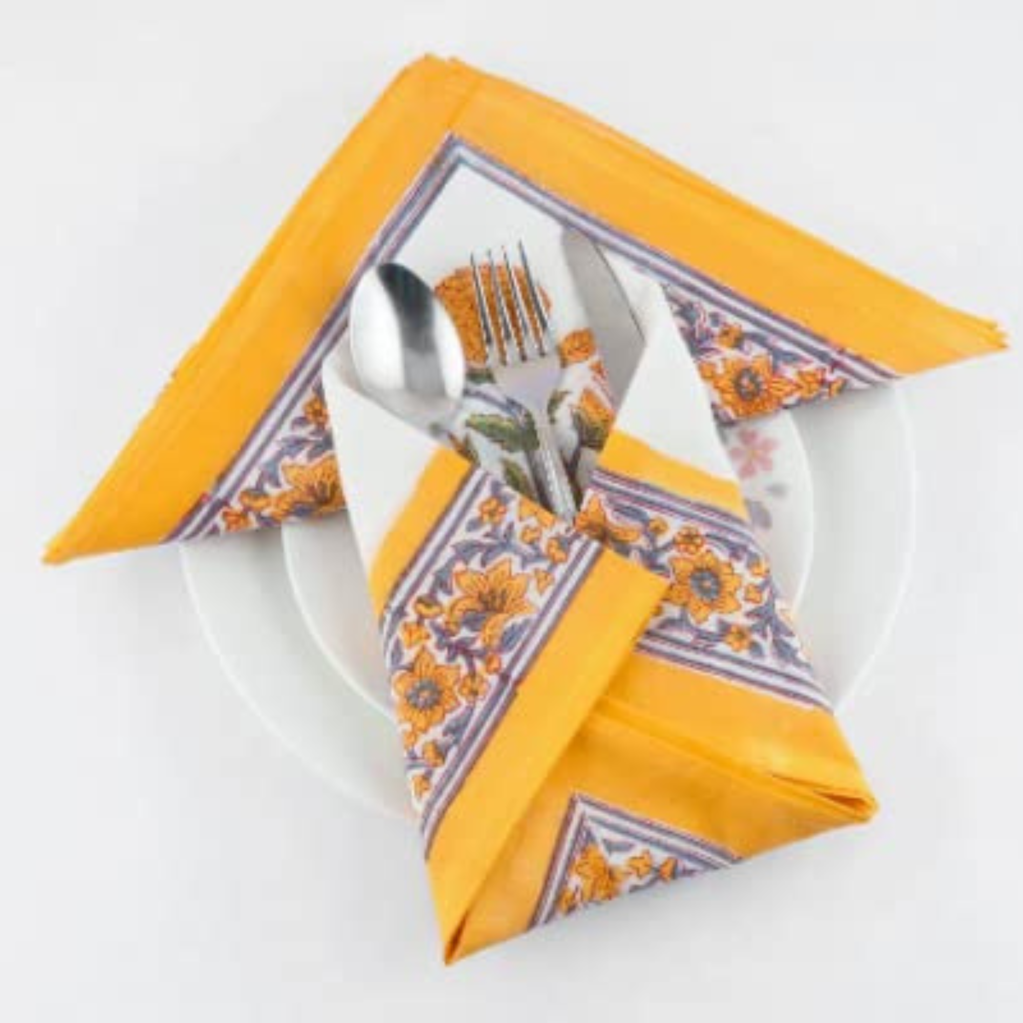 Decorative napkin with floral pattern and folded corners holding a fork, spoon, and knife on a white plate.