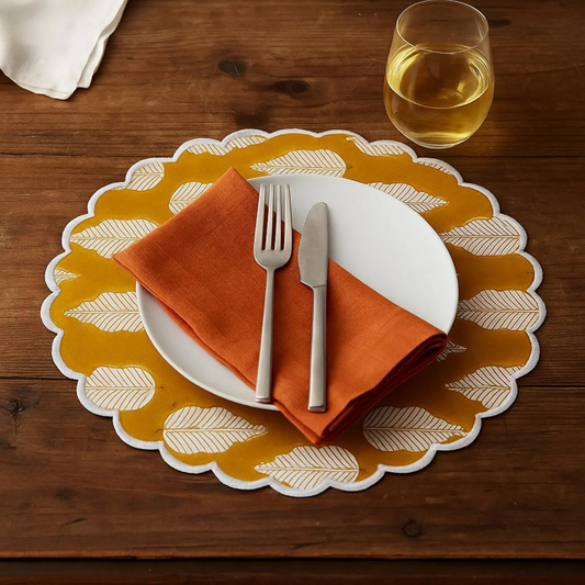 Dining setup with a yellow placemat, white plate, orange napkin, silverware, and a glass of white wine on a wooden table.